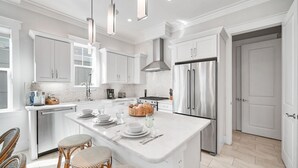 A modern kitchen with white cabinetry, stainless steel appliances, and a central island with seating. - Someday Came 4 Bedroom Home by RedAwning (Panama City Beach)