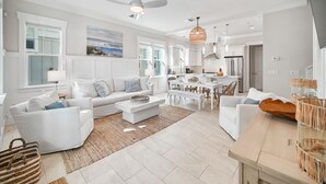A spacious living room with a white sofa, a dining table, and a kitchen area in the background. - Someday Came 4 Bedroom Home by RedAwning (Panama City Beach)