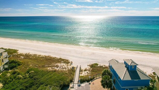 A beach view with a clear sky, a sandy beach, and a building with a blue roof. - Someday Came 4 Bedroom Home by RedAwning (Panama City Beach)