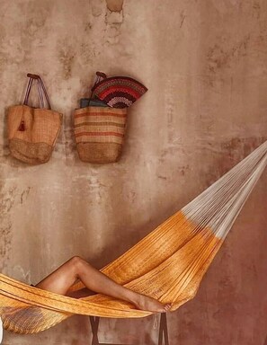 Un fauteuil suspendu en forme de hamac, dans lequel est assis une personne, le tout placé devant un mur à texture.