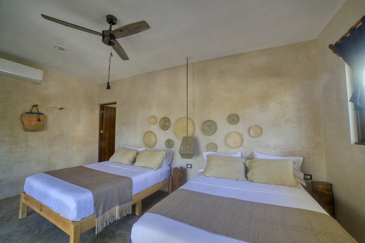 A room with two beds, a ceiling fan, and a wall decorated with woven baskets.