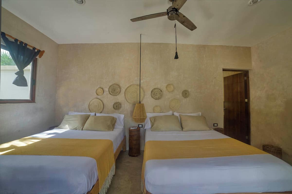A room with two beds, a ceiling fan, and a wall decorated with woven circular patterns.