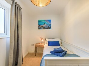 A bedroom with a bed, a nightstand, a lamp, a painting, and a window with curtains.