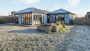A two-story house with a covered patio area, a fenced yard, and a gravel driveway. - Marram Dune Beach House (Brean)