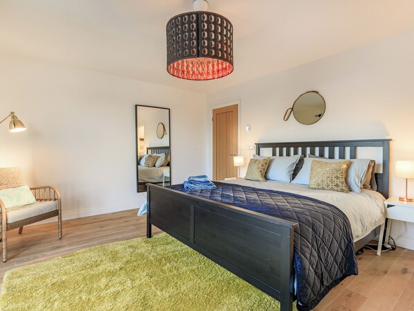 Un dormitorio con cama, mesitas de noche, un espejo y una lámpara colgante.