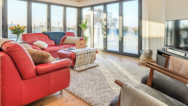 A spacious living room with a red sofa, a coffee table, and a TV. - Marram Dune Beach House (Brean)