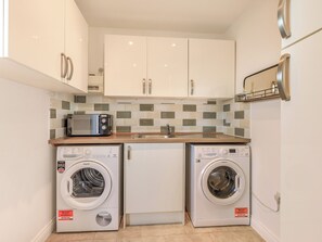 Una cocina compacta con microondas, dos lavadoras, un lavadero y salpicadero de azulejos.