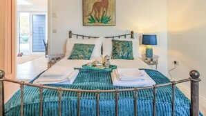 A neatly made bed with a blue bedspread and two pillows, a small table with a lamp, and a painting of a cheetah on the wall. - Marram Dune Beach House (Brean)