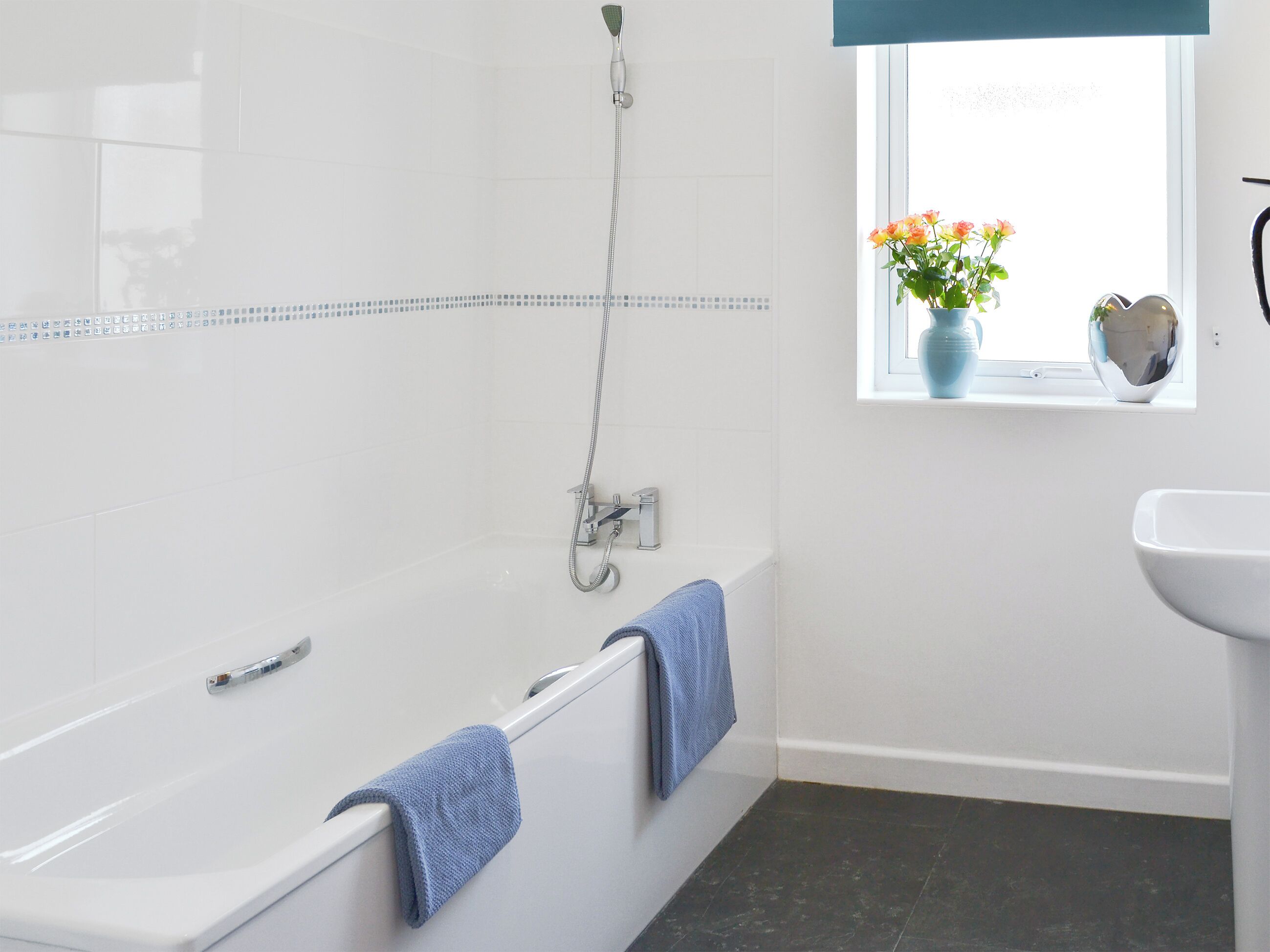 A bathroom with a bathtub, a window with flowers, and a sink.