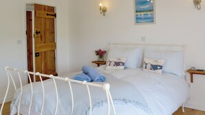 Ein Bett mit weißem Metallgestell und blauer Bettwäsche, eine Holztür, ein kleiner Nachttisch mit Lampe und ein Bild an der Wand.
