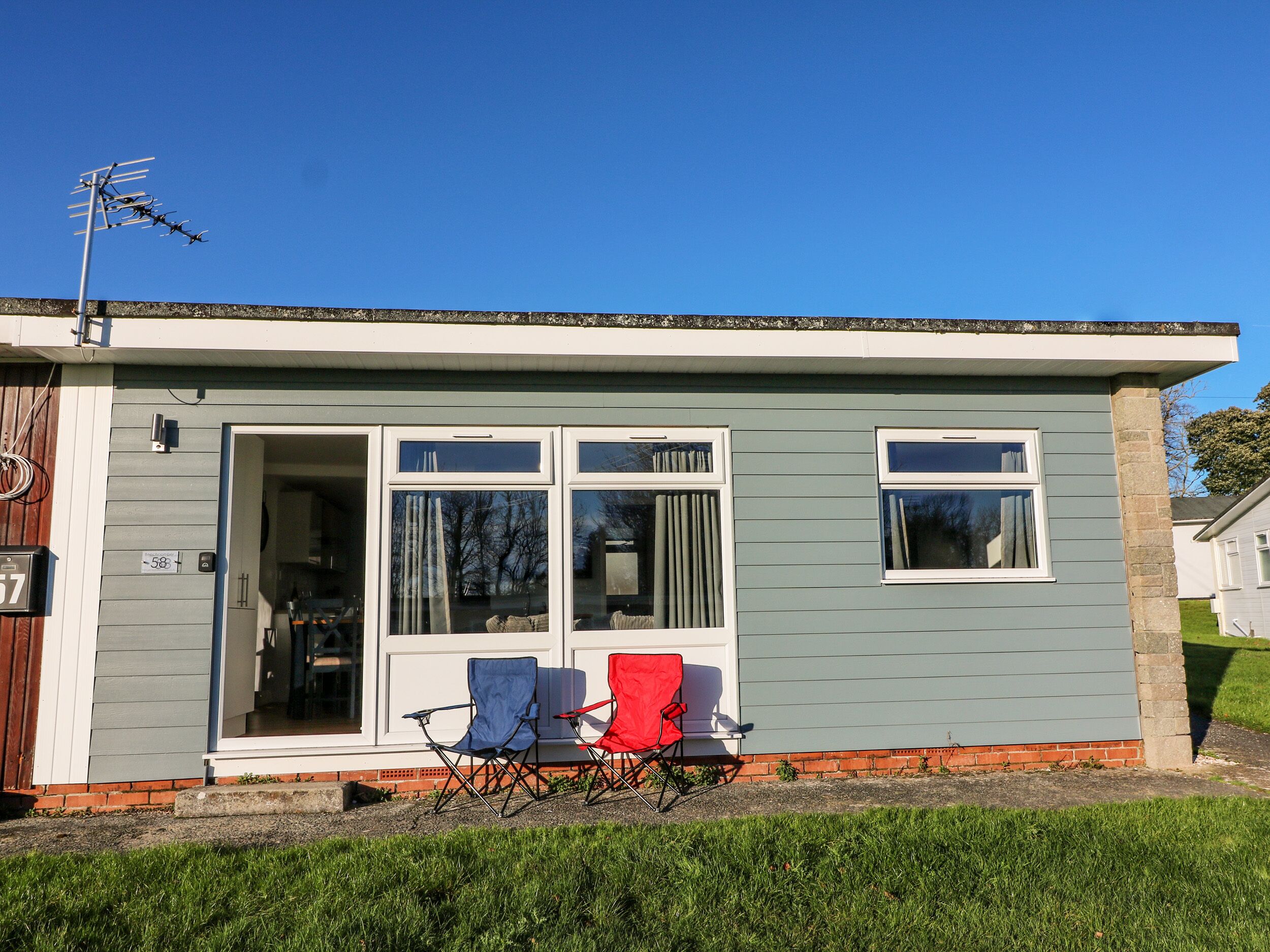 A single-story house with a grey exterior, a front door, and a small porch with two folding chairs.