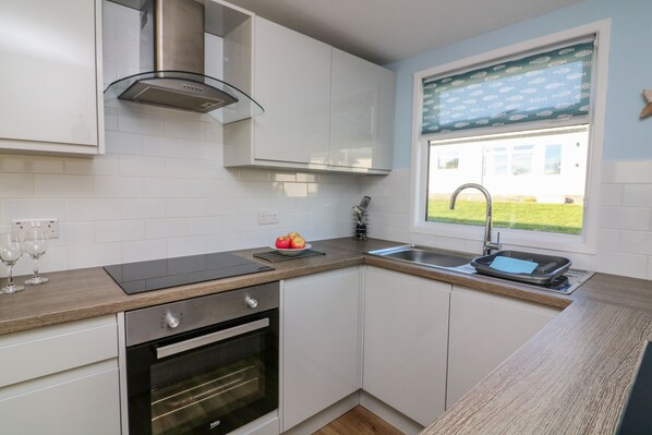 A modern kitchen with white cabinets, a built-in oven, a stainless steel range hood, a window with a view of a house, and a wooden countertop.