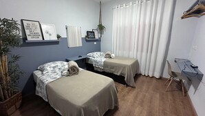 A bedroom with two beds, a desk, and a chair. There are wall decorations and a potted plant.