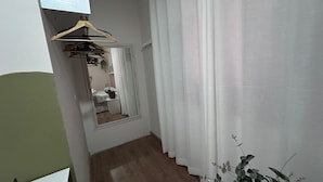 A hallway with a wooden floor, a mirror, a hanging clothes rack, and a white curtain.