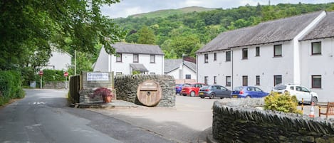 A rural street with a stone wall, a sign for Quaysiders Apartments & Hotel Rooms, and parked cars.