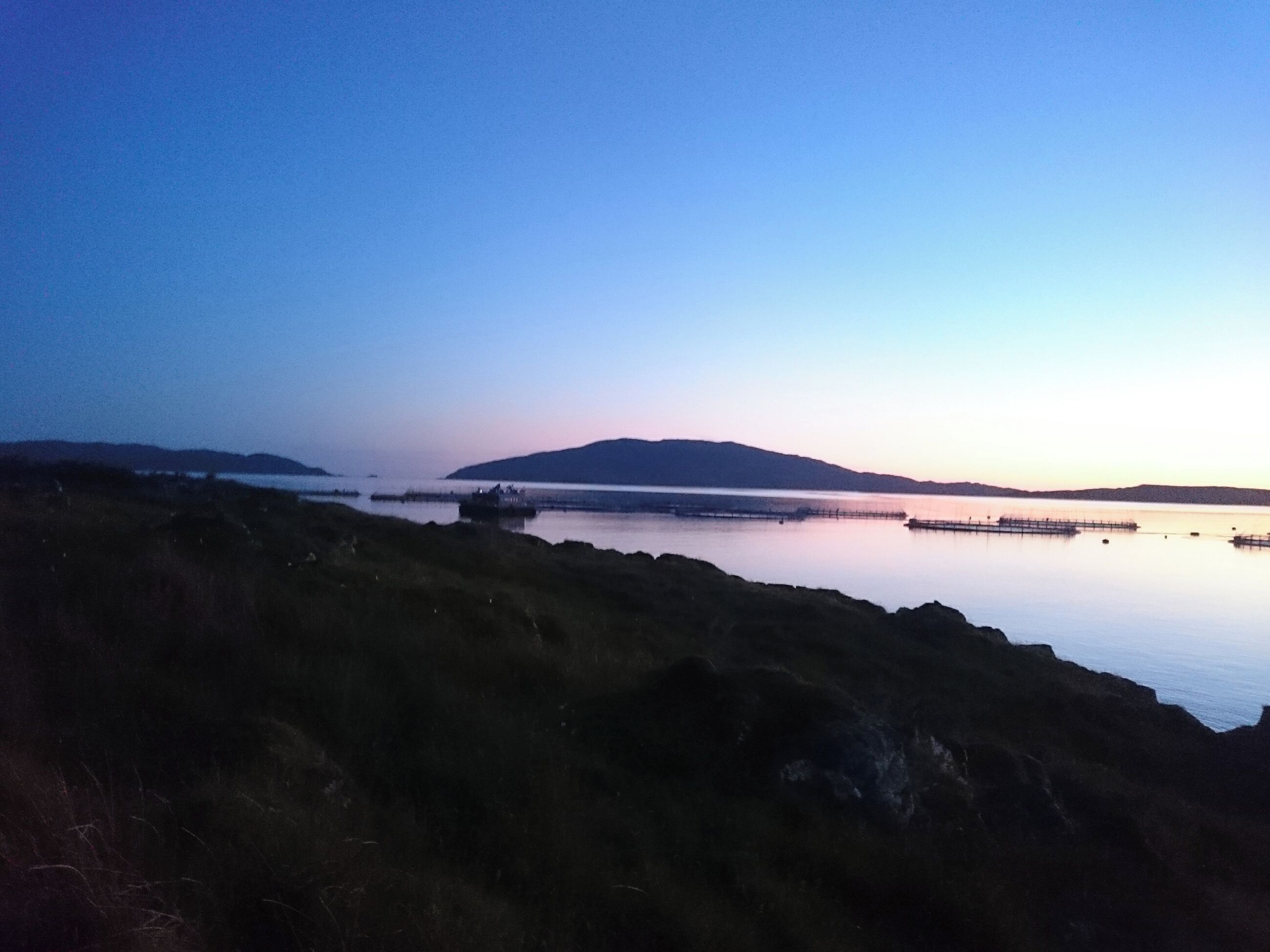 A coastal landscape with a calm sea, distant hills, and a clear sky.