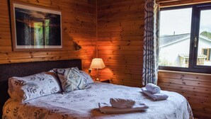 Une chambre rustique en bois, avec un lit, une table de chevet, une lampe et une fenêtre avec des rideaux.