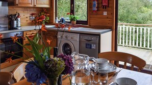 Une cabane avec un intérieur en bois, un lave-linge, une table à manger avec couverts et une vue sur les arbres.