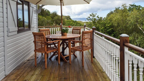 Une terrasse en bois avec une table et des chaises, un parasol et une rambarde.