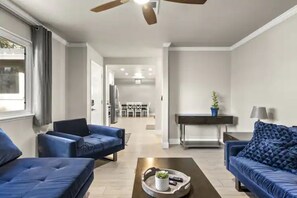 Un salón moderno con dos sofás azules, una mesita de centro con una bandeja y un ventilador de techo.