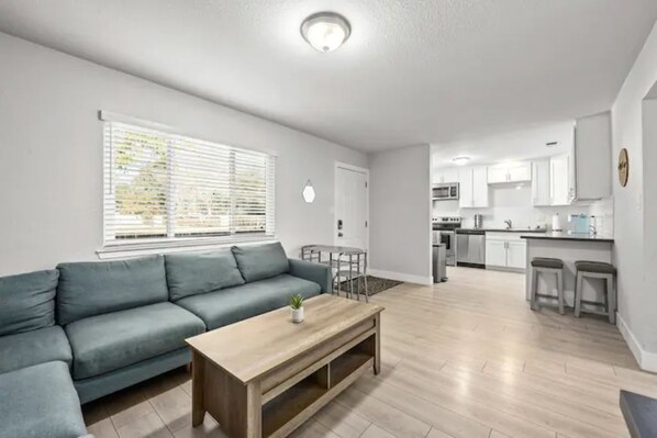 A modern living room with a sofa, a coffee table, and a kitchen in the background.