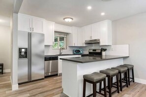 A modern kitchen with white cabinets, stainless steel appliances, and a central island with bar stools.