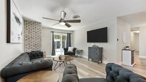 Ein modernes Wohnzimmer mit einer Eckcouch, einem runden Couchtisch und einem Deckenventilator.