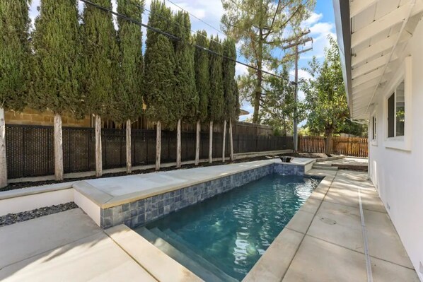 A swimming pool with a tiled edge, surrounded by a concrete deck and a wooden fence.