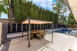 An outdoor patio with a covered dining area, a pool, and a wooden fence.