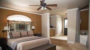 A bedroom with a bed, bedside tables, a ceiling fan, and a view of the bathroom.