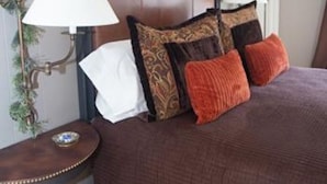 Una cama bien hecha con cabecera de madera, dos lámparas de noche y una mesita con un adorno decorativo.
