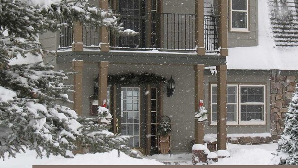 A two-story house with a stone facade, multiple windows, and a snow-covered roof.