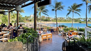 An outdoor dining area with wooden tables and chairs, overlooking a beach and palm trees. - Oceanfront 2BR 2BA Villa   Top-Floor Corner    Walk to Disney Aulani    Sleeps 6 (Kapolei)