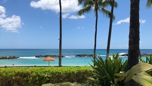 A beach view with palm trees, a wicker lounge chair, and a thatched umbrella. - Oceanfront 2BR 2BA Villa   Top-Floor Corner    Walk to Disney Aulani    Sleeps 6 (Kapolei)