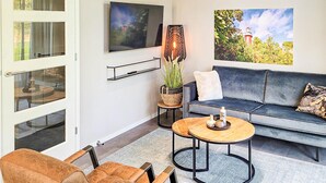 Een moderne woonkamer met een bank, twee fauteuils, een televisie, een lamp en een schilderij.