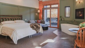 Een slaapkamer met een groot bed, een bank, een badkuip en uitzicht op de omgeving.