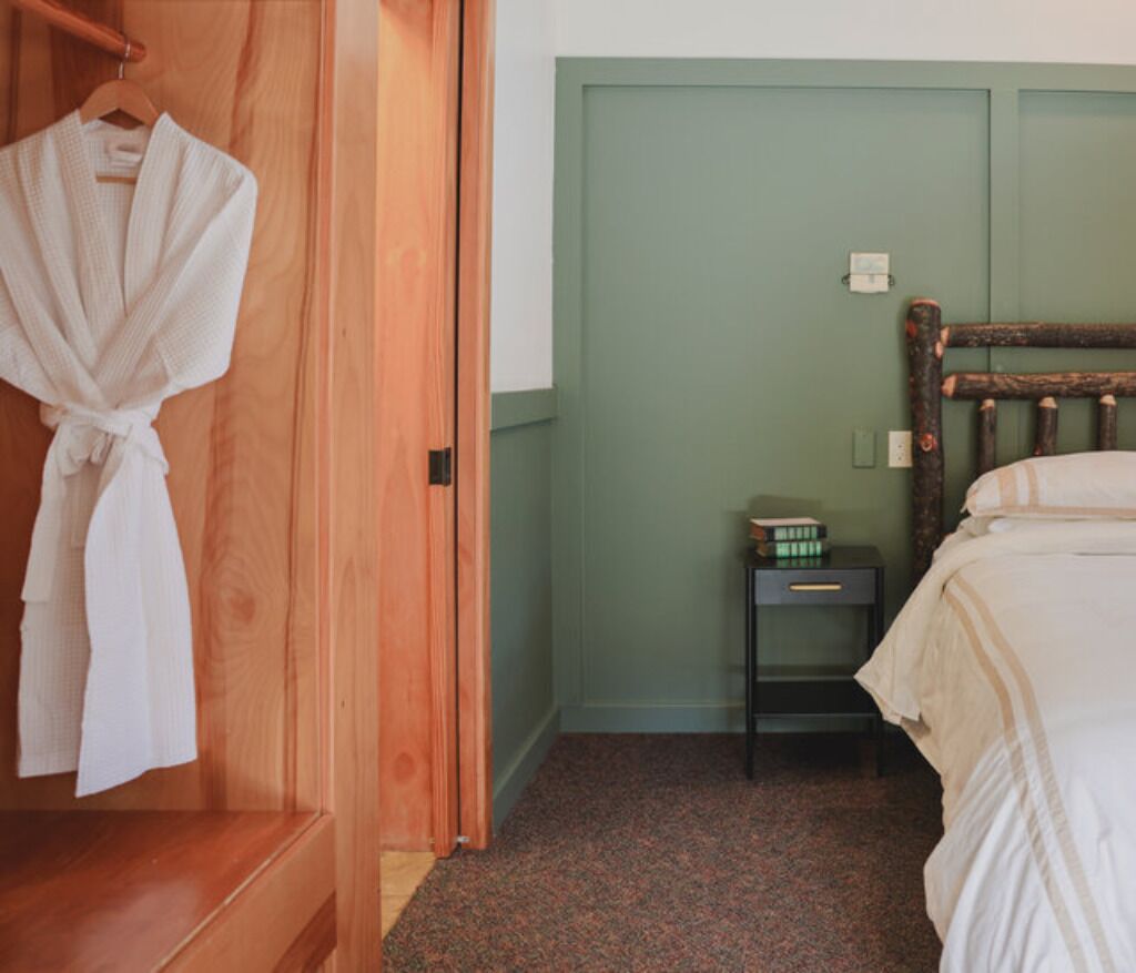 Ein Schlafzimmer mit einem hölzernen Kleiderschrank, einem Nachttisch mit Büchern und einem Bett mit weißer Bettwäsche.