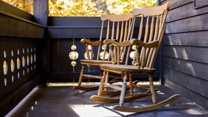 Een houten schommelstoel op een veranda met uitzicht op herfstkleuren.