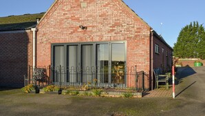 A red brick building with a large glass door, a metal fence, and a small garden area with flowers. - 1 bedroom accommodation in Doddington, near Lincoln (Doddington, near Lincoln)