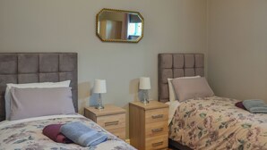 A bedroom with two beds, a nightstand with lamps, a mirror, and a wooden drawer unit. - 1 bedroom accommodation in Doddington, near Lincoln (Doddington, near Lincoln)