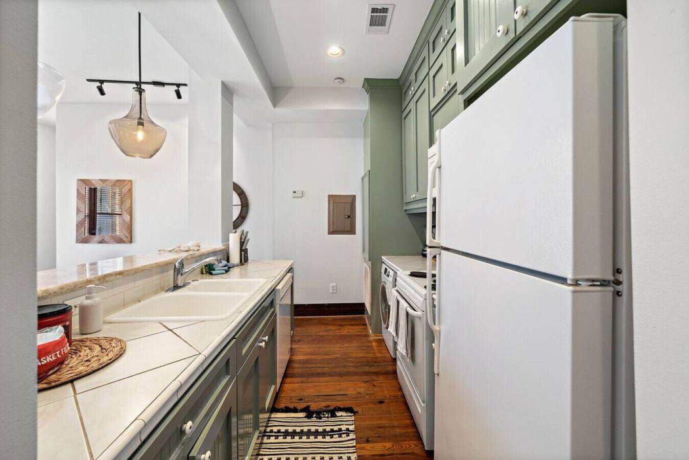 A kitchen with white cabinets, a stainless steel refrigerator, a wooden floor, and a hanging pendant light.