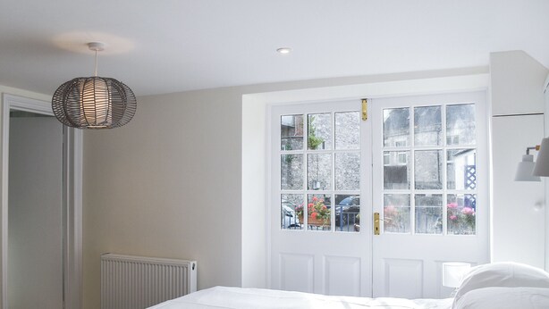 A bedroom with a bed, a radiator, a window with a view of the outside, and a hanging light fixture. - 3 bedroom accommodation in Swanage (Swanage)