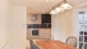 A modern kitchen with stainless steel appliances, a wooden dining table, and a view of the outside. - 3 bedroom accommodation in Swanage (Swanage)