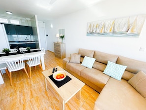 A modern living room with a beige sofa, a dining table with chairs, and a kitchen in the background.