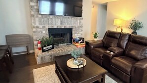 A living room with a fireplace, a leather couch, a coffee table, and a TV mounted above the fireplace. - Beautiful San Antonio Home near SeaWorld/Six Flags (San Antonio)