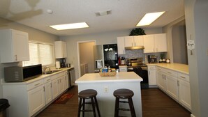 A modern kitchen with white cabinets, a central island with stools, a microwave, and a refrigerator. - Beautiful San Antonio Home near SeaWorld/Six Flags (San Antonio)