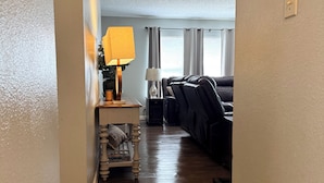 A hallway leading to a living room with a sofa, a lamp, and a small table. - Beautiful San Antonio Home near SeaWorld/Six Flags (San Antonio)