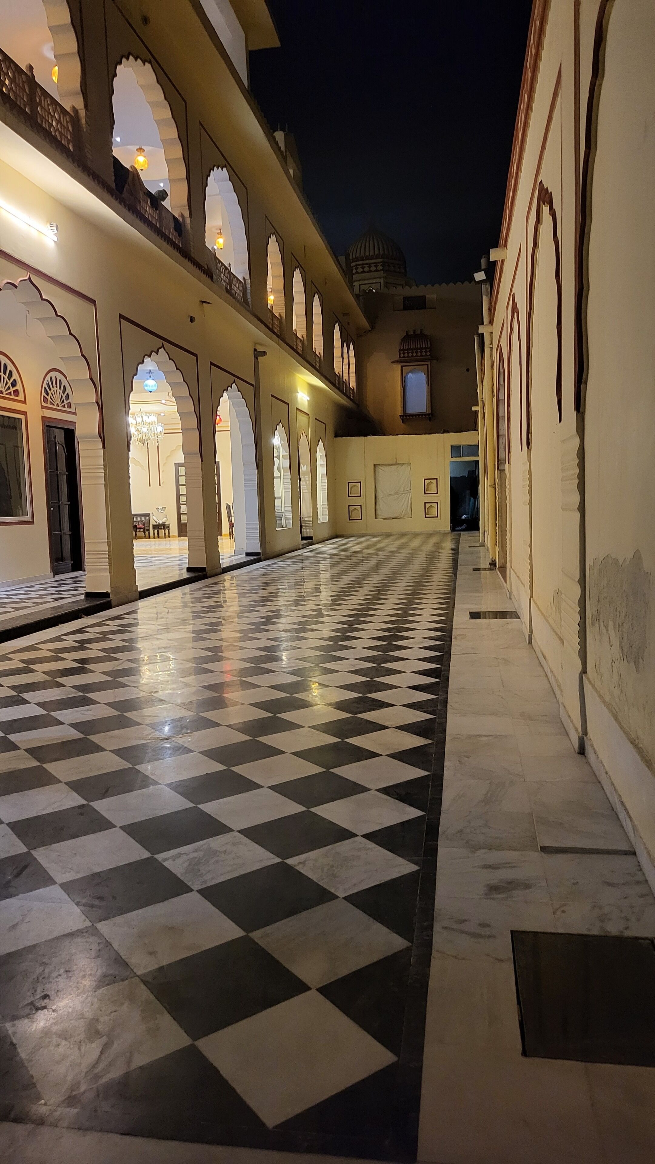 A corridor with a checkered floor, arched doorways, and a domed structure in the background.