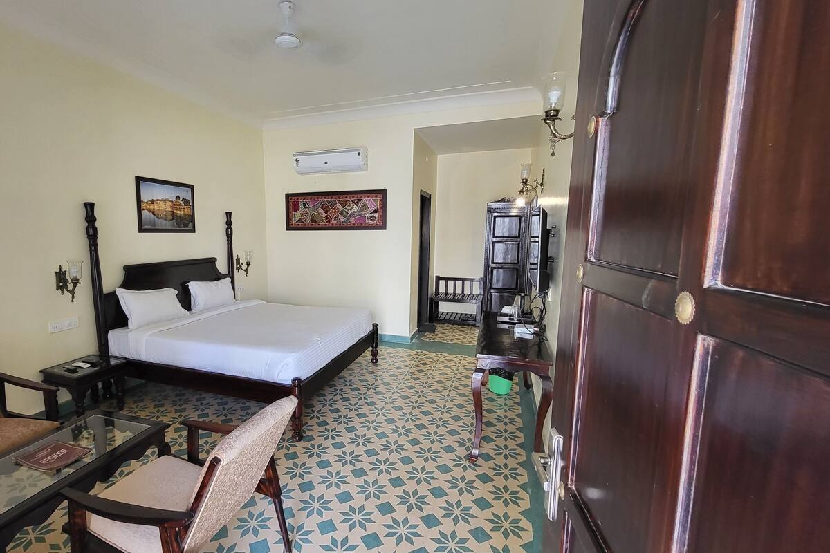 Una habitación de hotel con cama, una silla, una mesita, una estantería y una puerta.