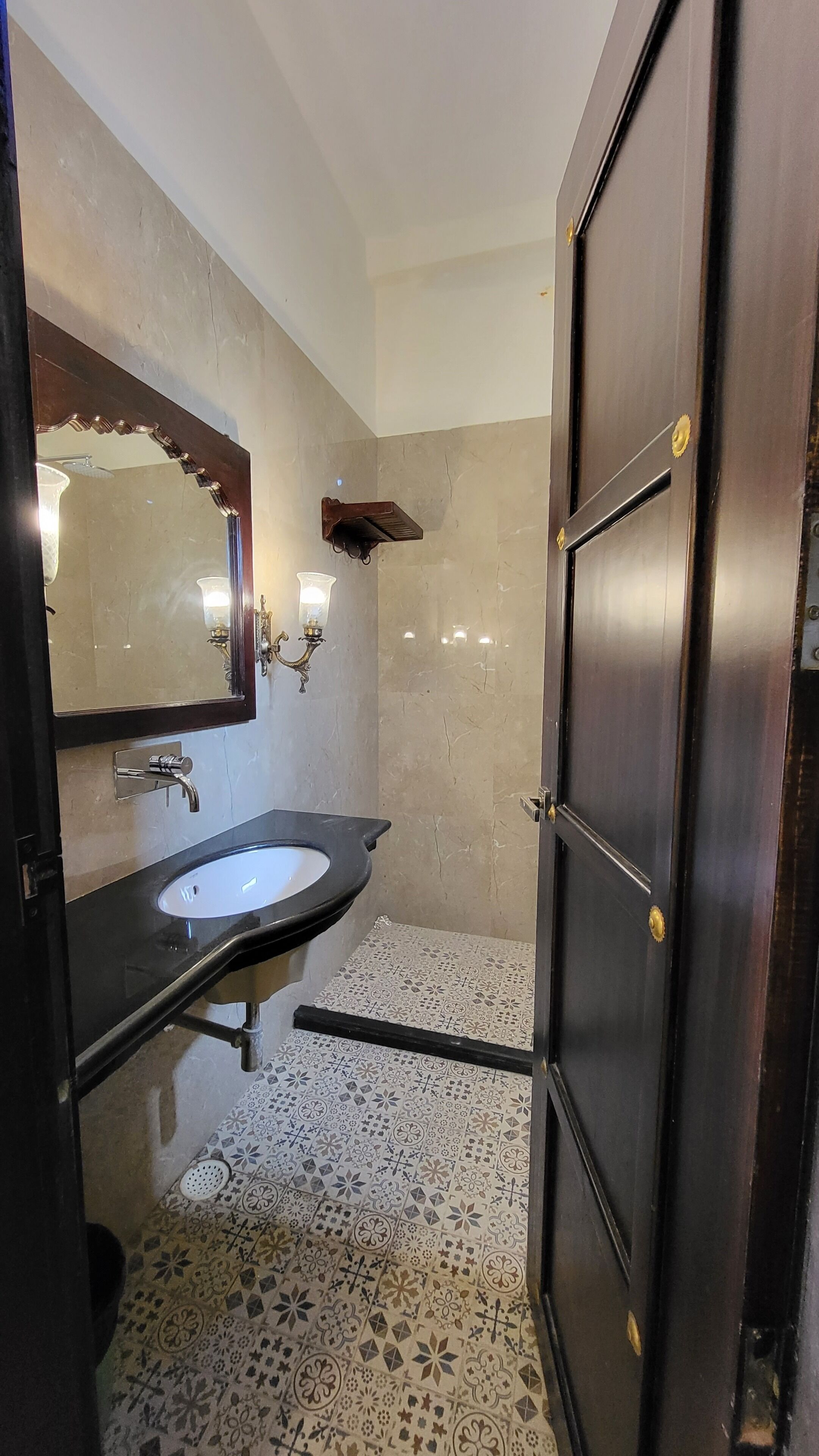 Un baño con pared de mármol, un lavabo con espejo, un perchero y una puerta.